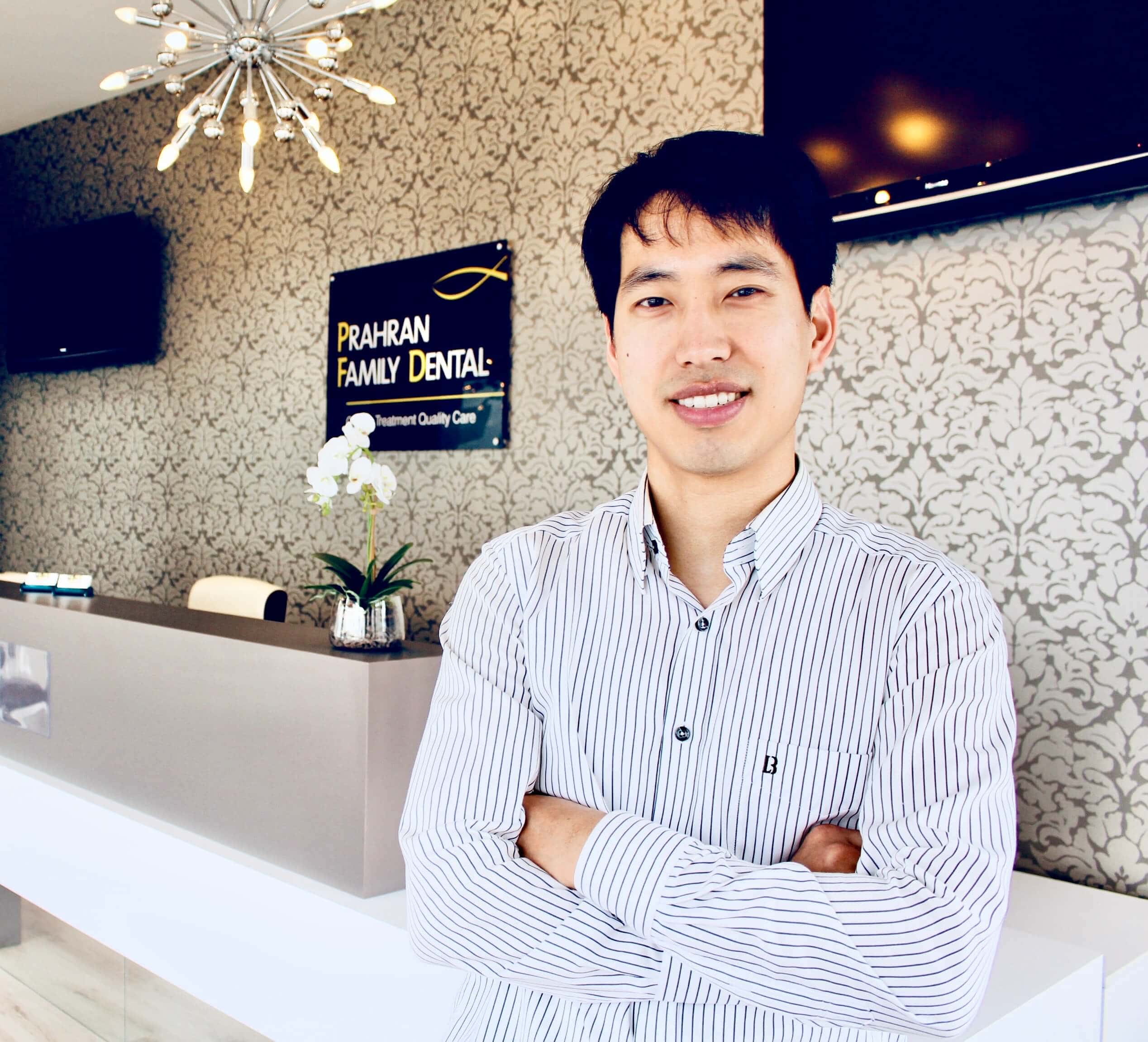 Dr Jun Kim principal dentist standing at the reception desk in Prahran
