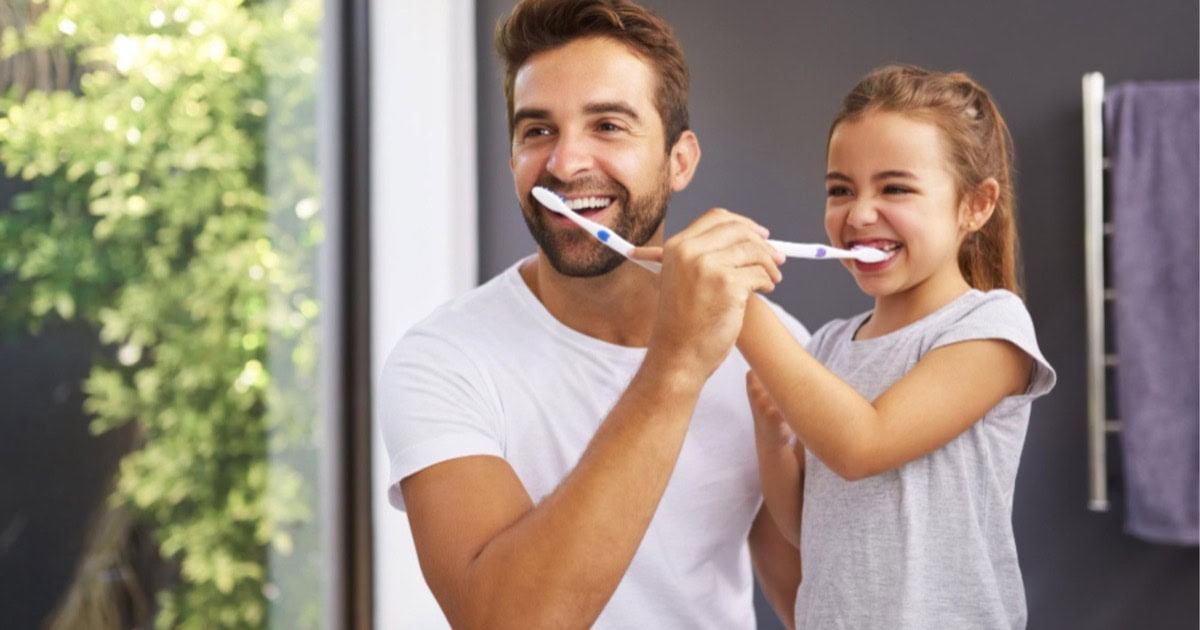 Father and daughter brushing their teeth together