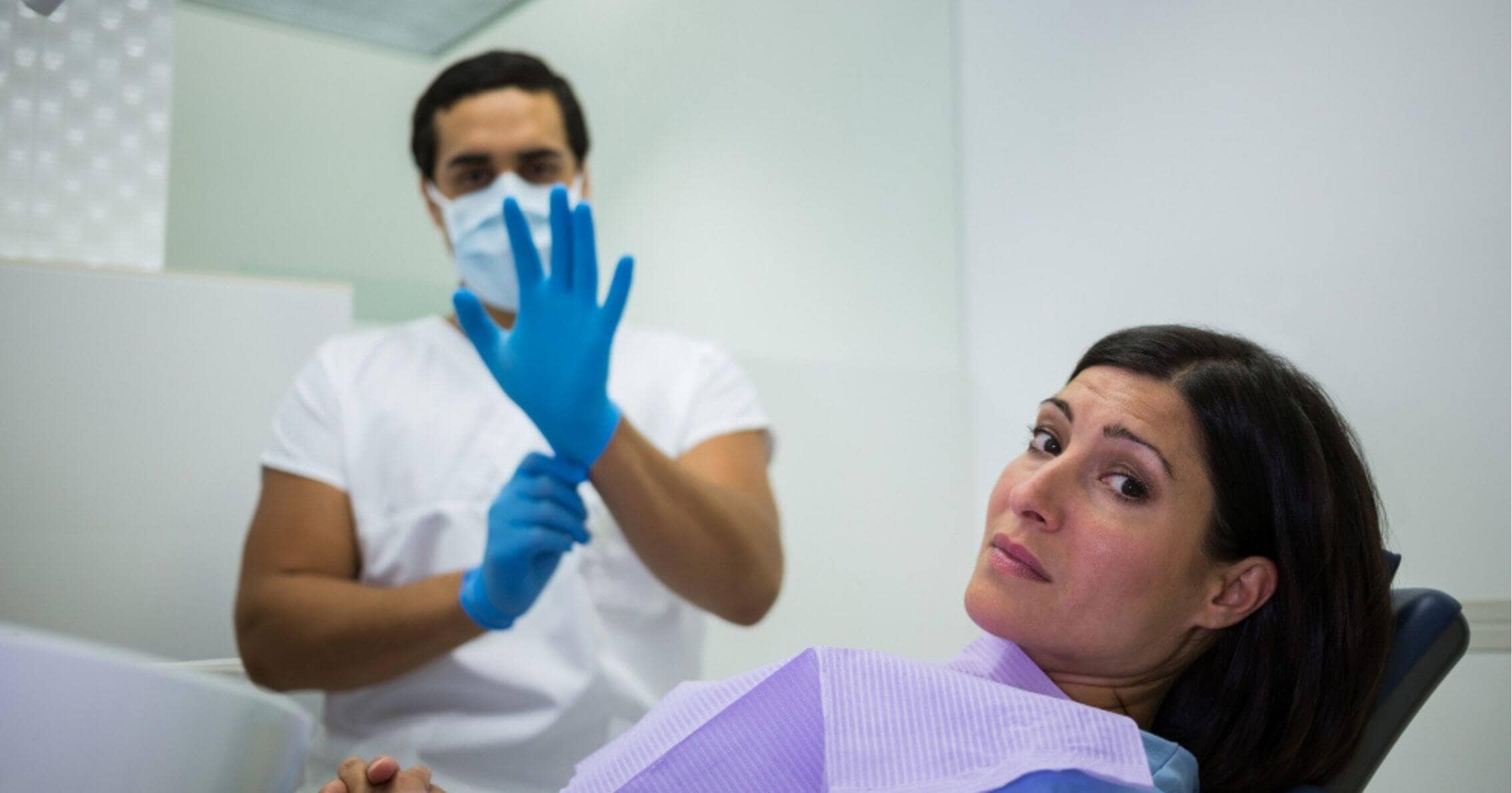 patient looking anxious in the dental chair while the dentist puts on gloves in Prahran